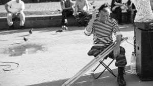 grayscale photo of man sitting on folding stool with crutches in front of people